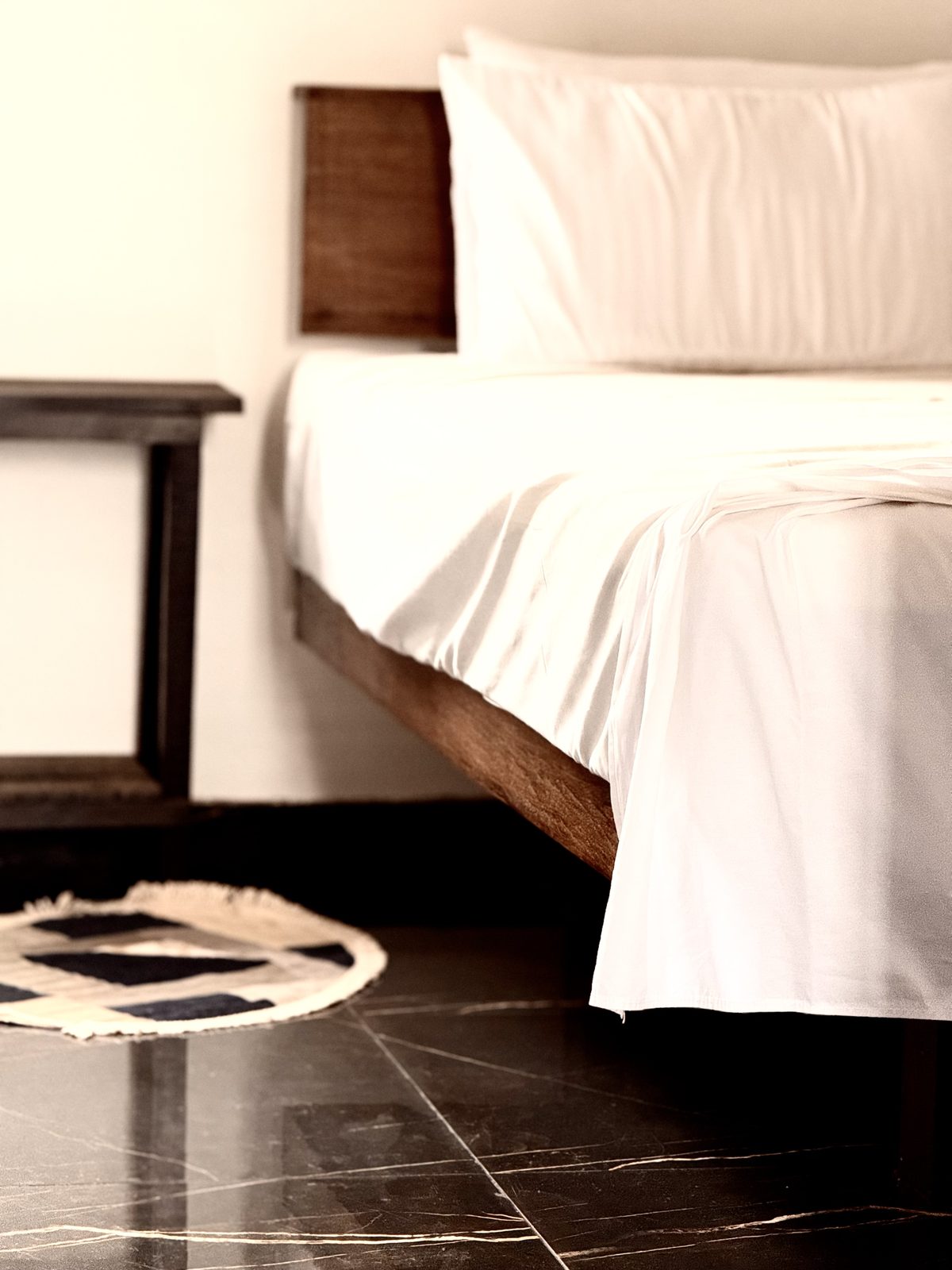 Detalhe da cama com roupa branca e mesa lateral de madeira no Studio do Hotel Holambra