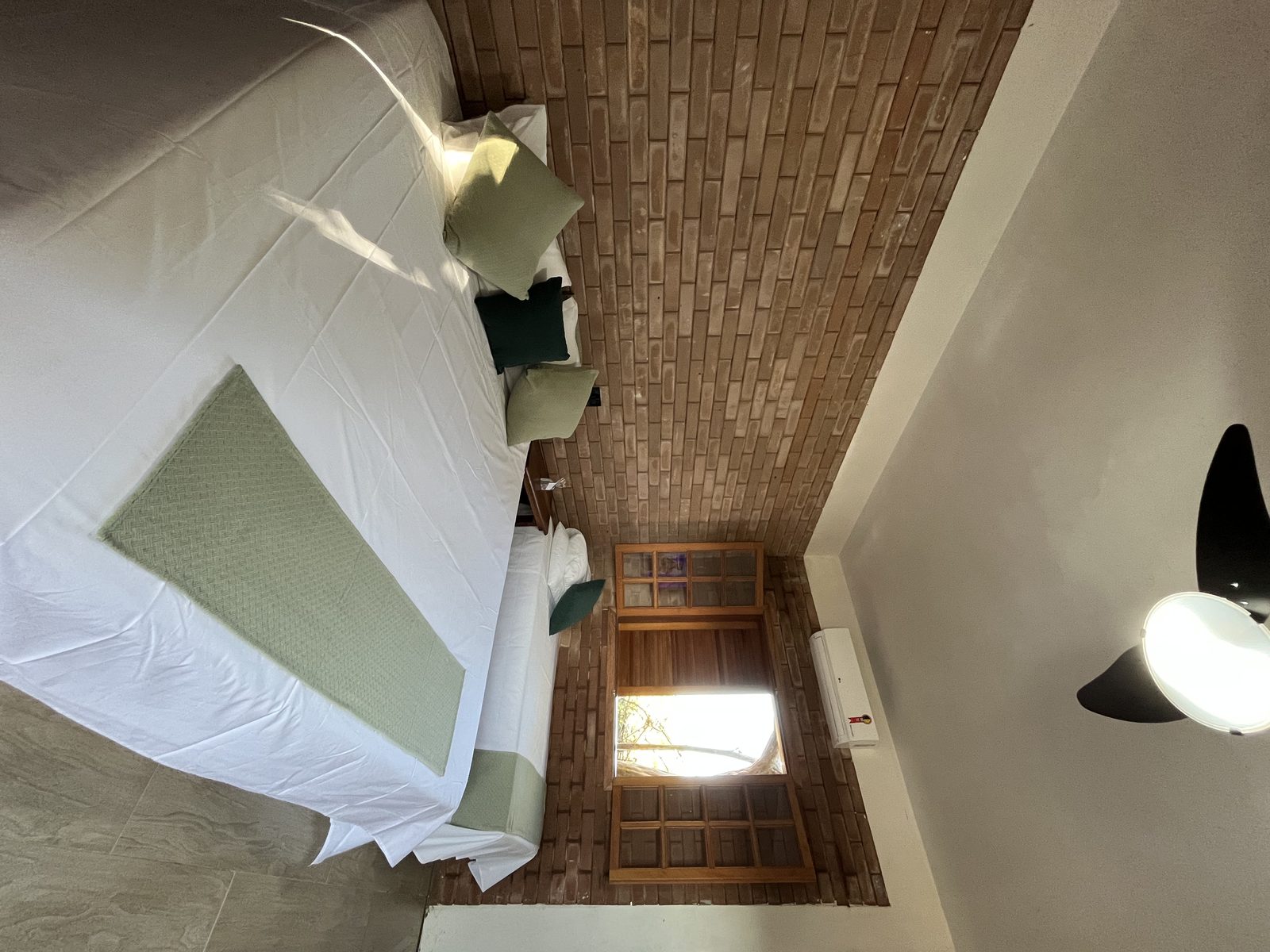 Cama de casal com almofadas verdes e porta de madeira com vista para o jardim na Suíte Família