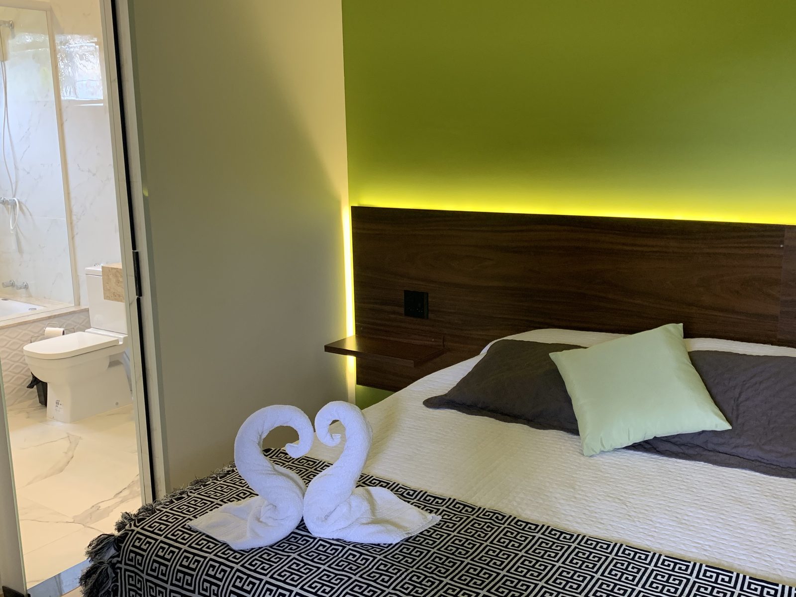 Cama de casal com toalhas decoradas em formato de cisnes e banheiro privativo ao fundo na Suíte Real